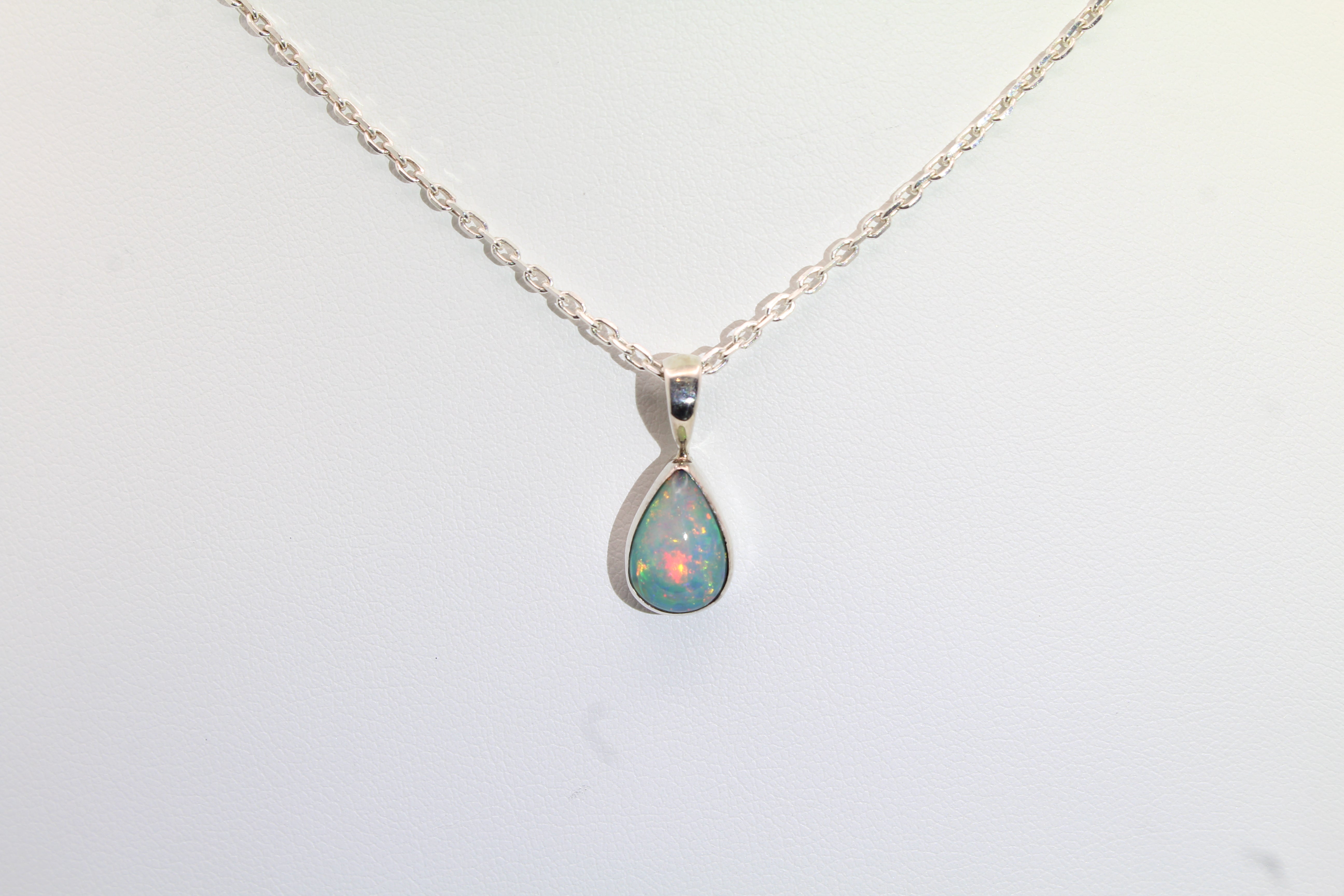 Teardrop-shaped opal pendant on a silver chain against a white background