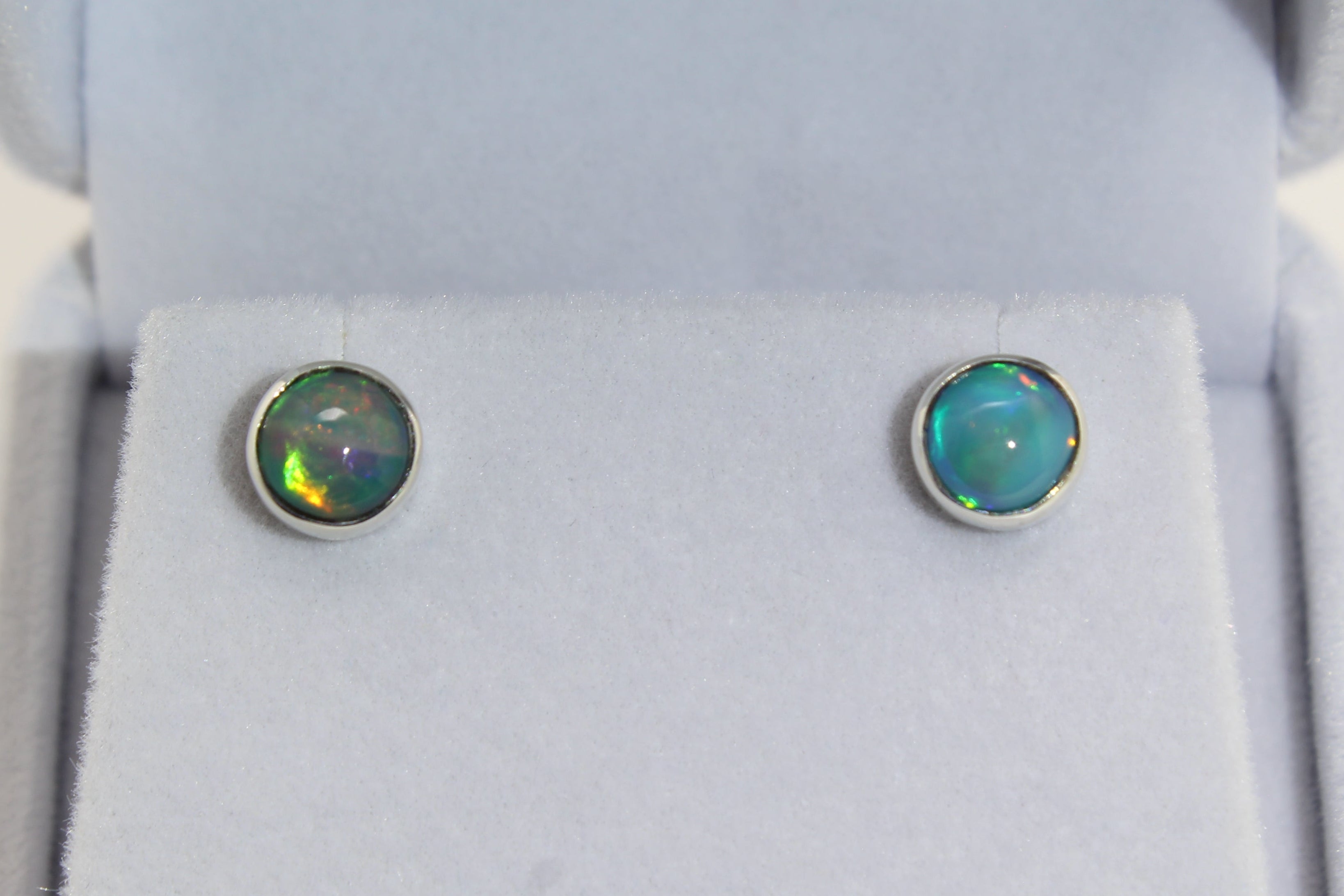 Pair of round silver opal earrings in a jewelry box
